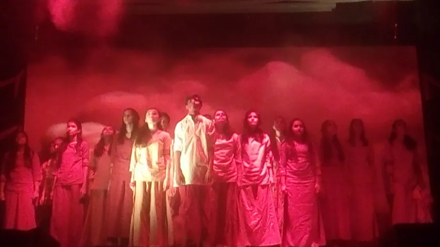 Large cast in white costumes standing under red stage light