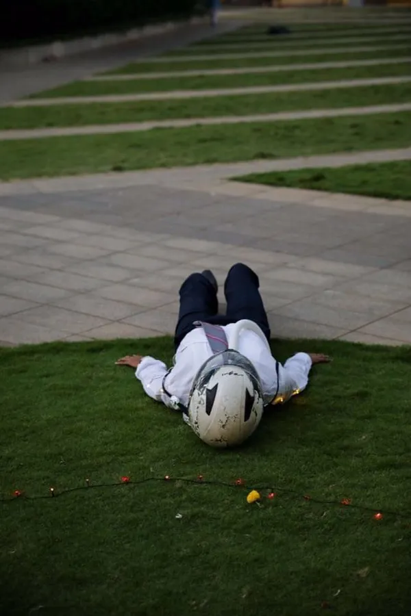 Performer in a white mask lying on the grass during an outdoor performance