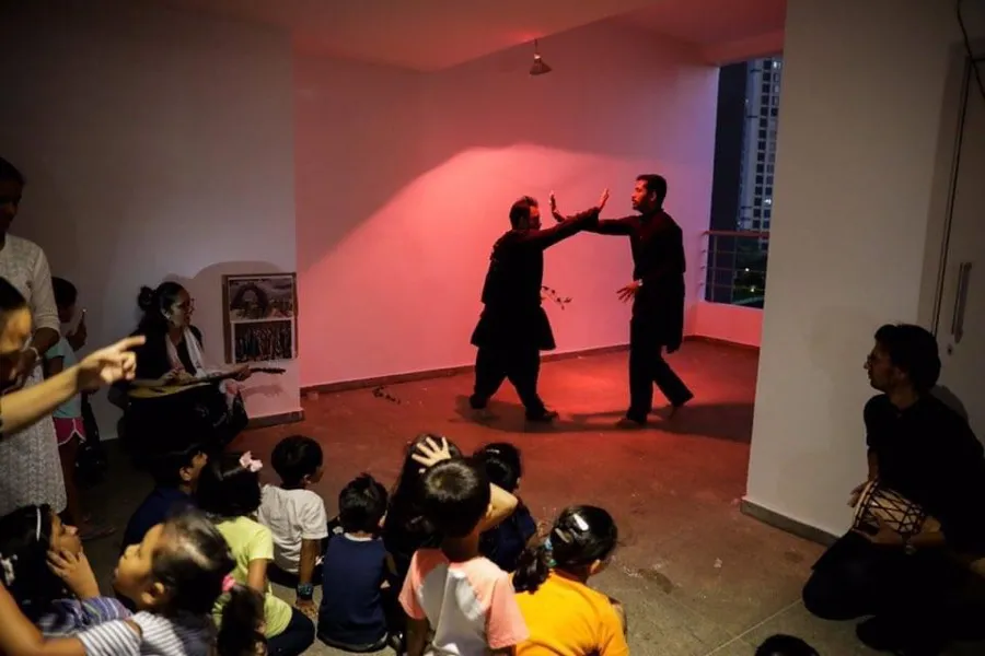 Two performers in black acting for children seated on the floor