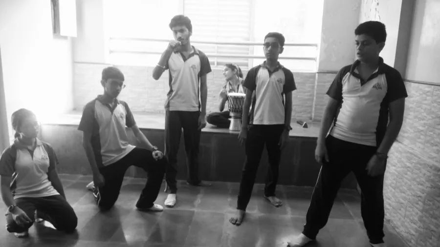 School students in a drama exercise beside a window, with a drum in the background