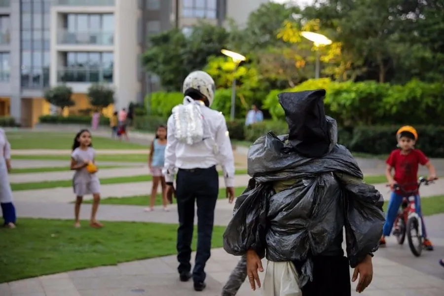 Masked performers walking through a housing compound as children watch