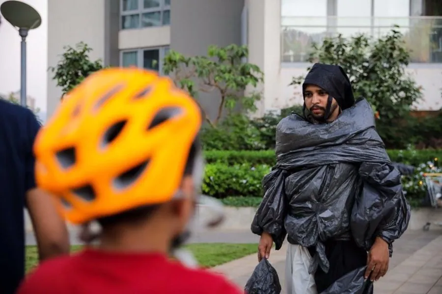 Performer wrapped in plastic sheeting during a street performance, a child watching in the foreground