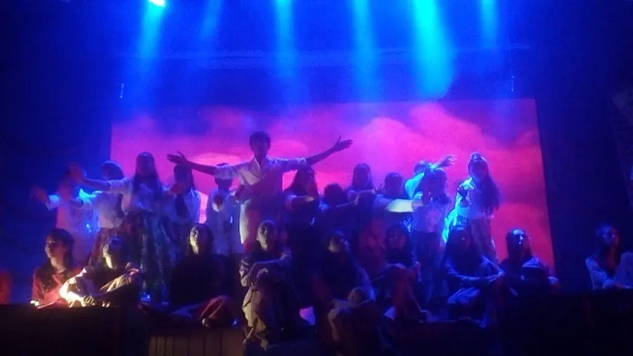 Large group performing with arms raised under blue stage light