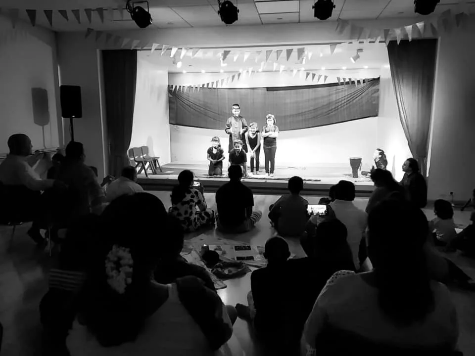 Children performing a Playback Theatre show on stage while the audience sits on the floor
